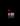 A small lit candle and its box on a glossy black surface against a black background. The candle features a white Buddha head on top of stacked pink, purple, and black candles.